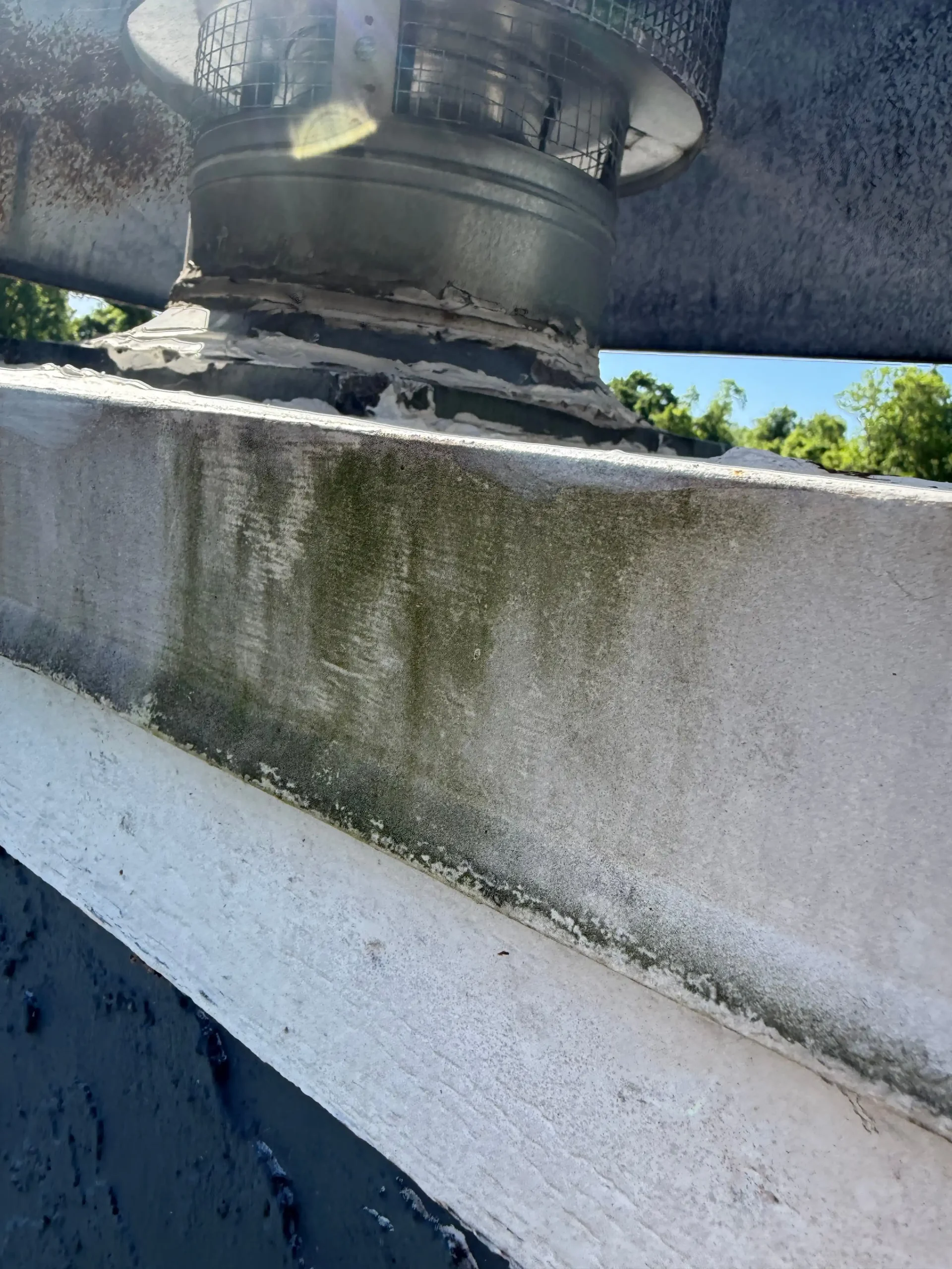 Damaged chimney cap with deteriorating mortar and algae staining on concrete surface