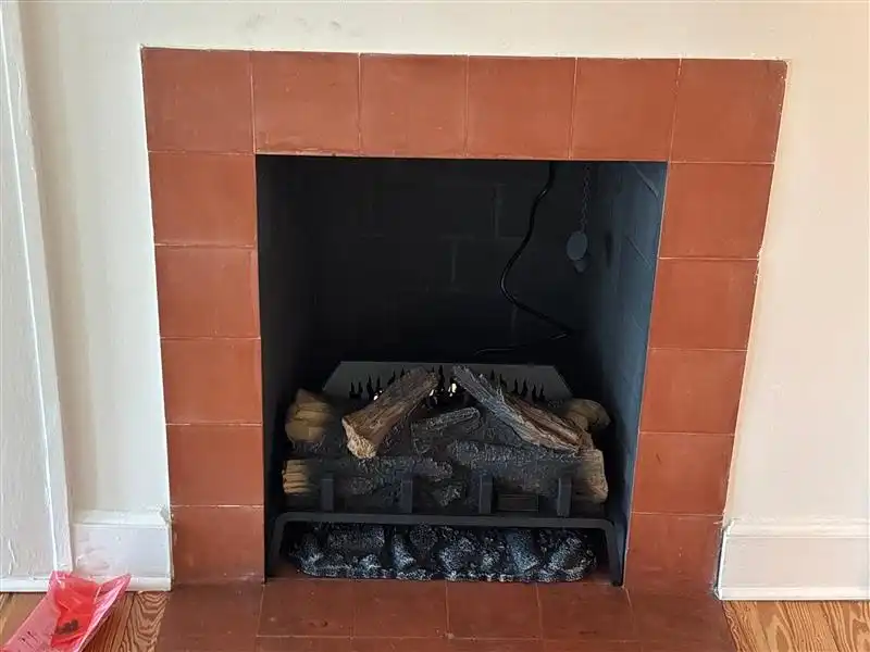 Electric fireplace insert with faux logs in terracotta tile surround