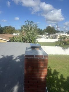 Brick chimney corner with a new galvanized cap on a flat roof near Bradenton Beach
