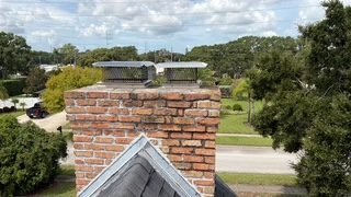 Aerial rooftop view of a brick chimney with two round mesh caps surrounded by oak trees near Osprey, FL