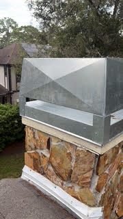 Aerial view of a stone-clad chimney with a new galvanized cap surrounded by oak trees near Osprey FL
